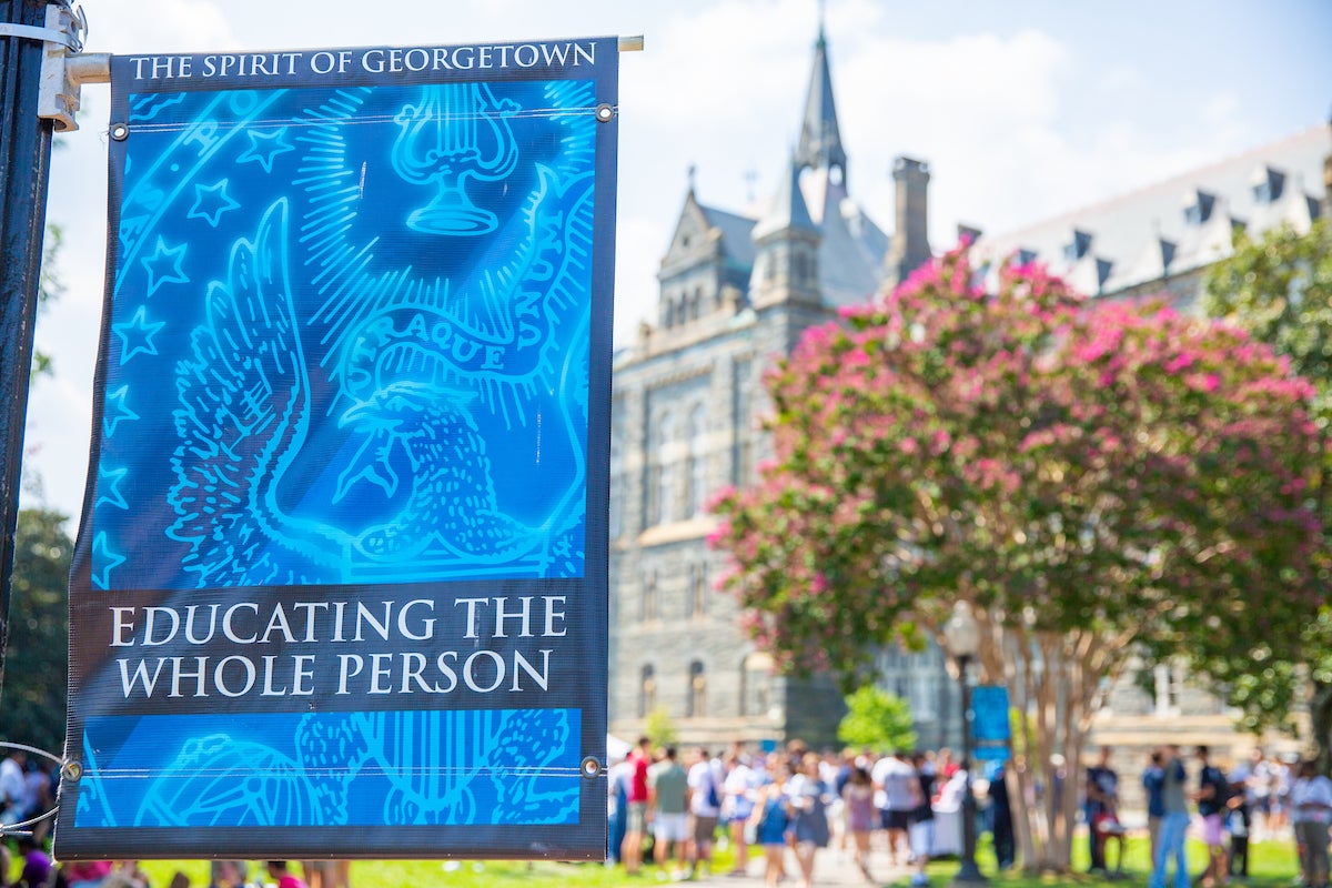 A banner outside Healy Hall reads "Educating the Whole Person". Students are visible on Healy Lawn.